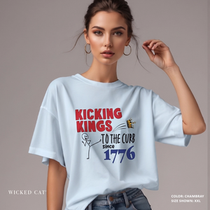 Woman wearing a light blue patriotic t-shirt with a graphic and text Kicking Kings to the Curb since 1776 on a gray background