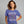 A woman wearing a periwinkle blue graphic t-shirt with a skeleton dancing amidst red and orange autumn leaves, with the text 'IT'S THE MOST WONDERFUL TIME OF THE YEAR'. The brand name 'Wicked Cat' is visible in the bottom-left corner.