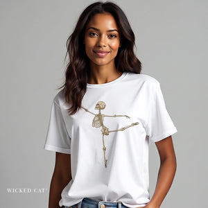 A woman wearing a white short-sleeve crewneck t-shirt with a graphic of a dancing skeleton on the front, paired with blue jeans, against a solid gray studio background. The brand name 'WICKED CAT' is printed in the bottom left corner.