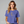 A woman wearing a periwinkle blue t-shirt with a skeleton graphic on the front, posed against a solid gray studio background. The brand name 'WICKED CAT' is printed in white in the bottom-left corner.