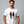 Man wearing a white t-shirt with a graphic design and text, standing against a gray background.