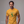 A man wearing a mustard yellow graphic t-shirt with a green cartoon alien and the text 'HELLO MY BABY' on the chest, set against a plain gray studio background.