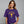 A woman wearing a purple short-sleeve t-shirt with a yellow and blue graphic of a skeleton figure and the text 'FUSILLI JERRY' on the front, set against a solid gray background.