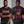 A man modeling a black graphic T-shirt shown from both front and back. The front has orange gothic-style text reading 'START JUMPING,' and the back has large distressed text reading 'SHAKE THE STADIUM' in purple and orange.