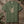 An olive green short-sleeve t-shirt with a graphic of a skeleton hand making the rock on gesture, displayed flat on a rustic wooden background with green leaves.