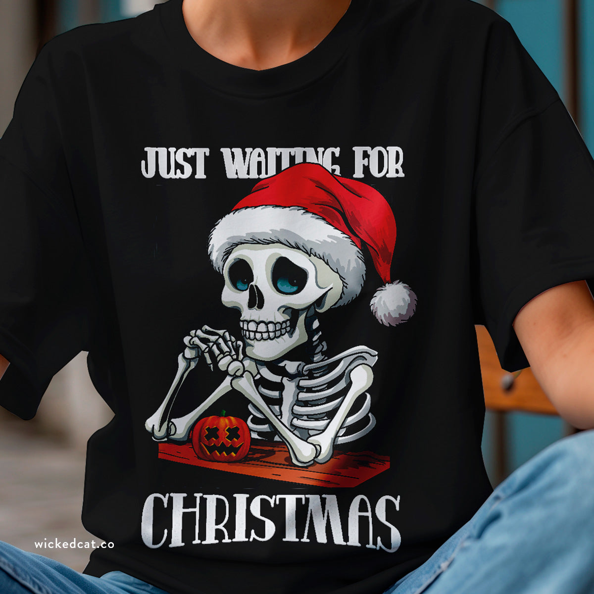 Black t-shirt with skeleton wearing a Santa hat and text 'Just Waiting for Christmas' on a white background