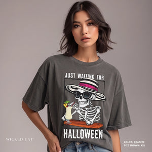Woman wearing a gray t-shirt with a skeleton and cat graphic and text 'Just Waiting for Halloween'.