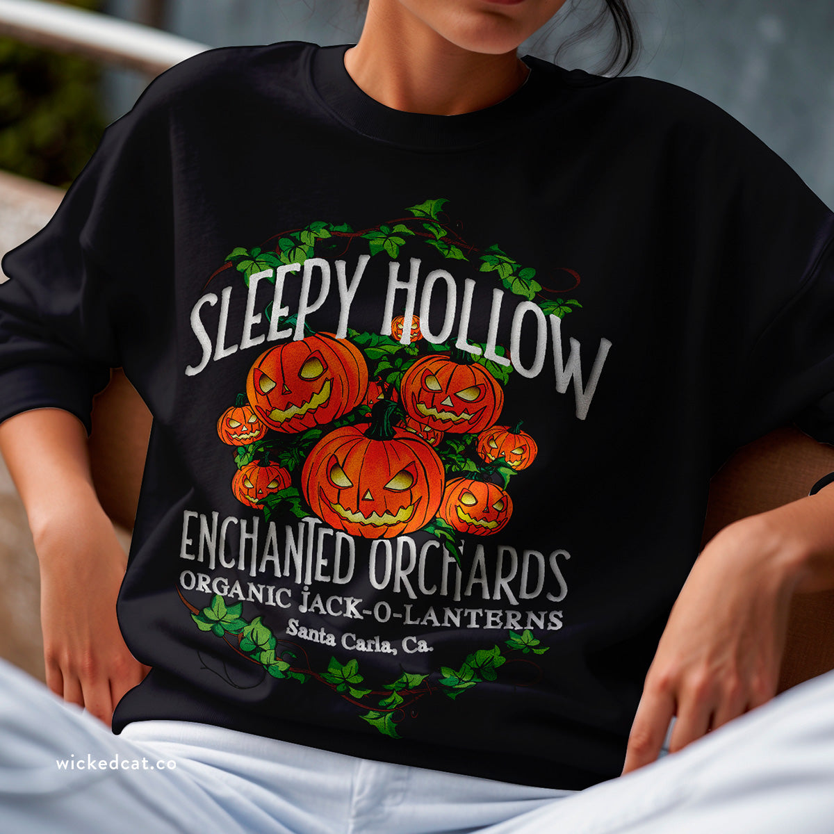 A navy crewneck sweatshirt with a graphic print of pumpkins and the text 'Sleepy Hollow Enchanted Orchards Organic Jack O Lanterns Santa Cruz, CA.'.